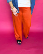 Person wearing orange pants and a blue jacket on a pink background